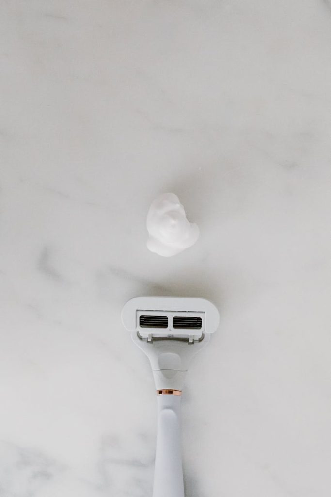 a white shaver and shaving foam on marble surface